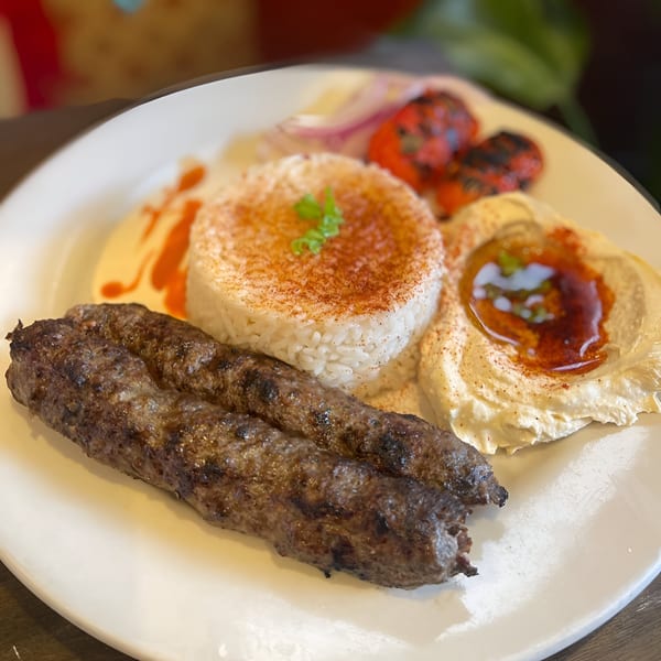 Lebanese kofta kebabs with rice, hummus, grilled tomatoes, and red onion on a white plate.