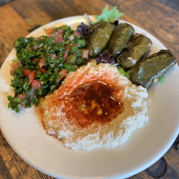 A white plate holds Lebanese hummus, tabbouleh, and stuffed grape leaves on a wooden table.