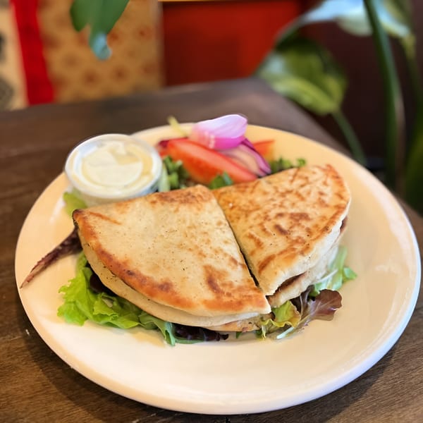 Two pita bread sandwiches with lettuce, tomato, onion, and a side of white sauce on a plate.